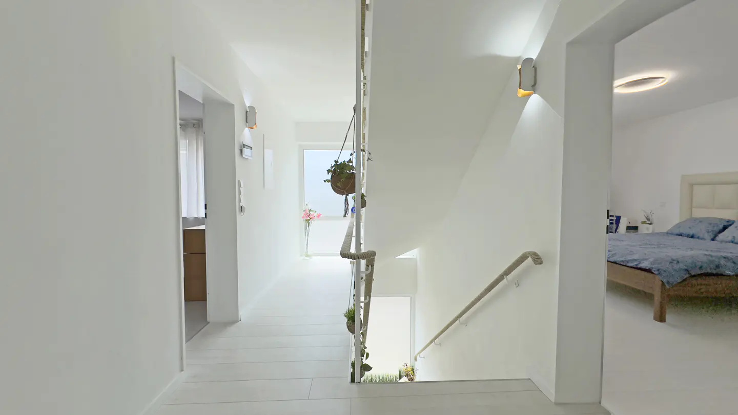 Bright white hallway with a staircase, hanging plants, and doorways leading to a bedroom and another room.