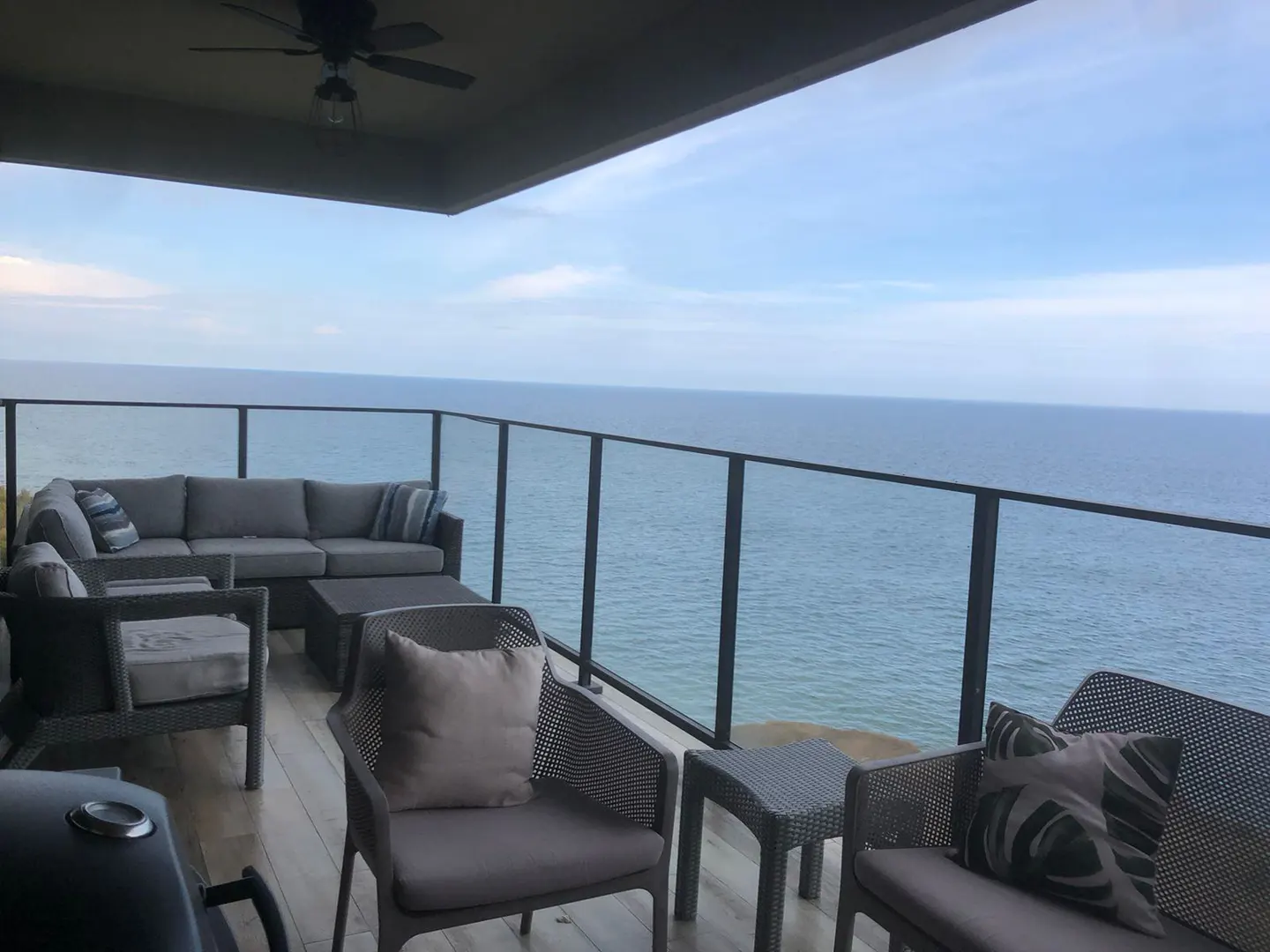 Outdoor patio with gray wicker furniture, glass railing, and ocean view.