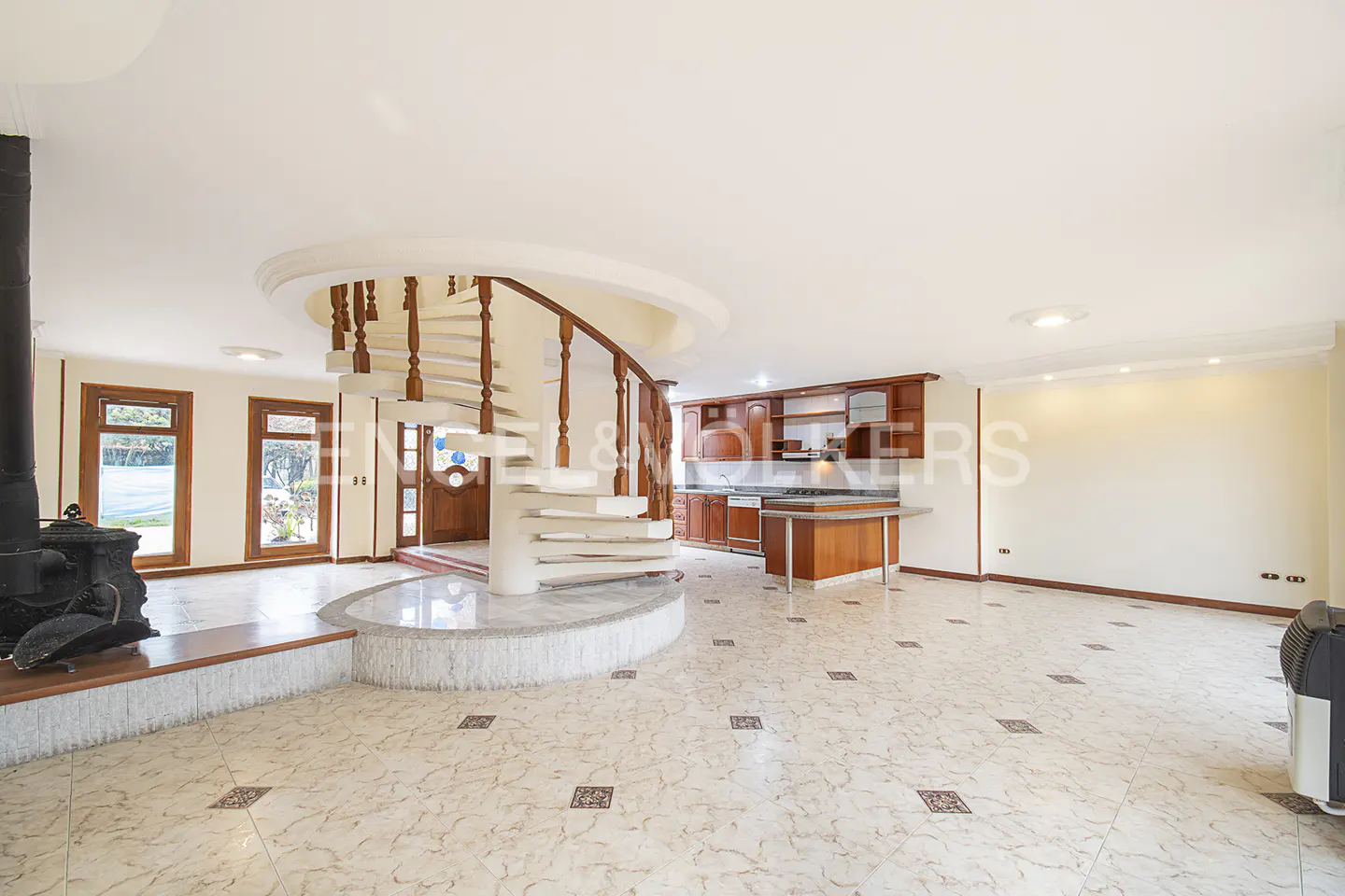 Open-concept living space with a spiral staircase, wood kitchen cabinets, and a black wood-burning stove.