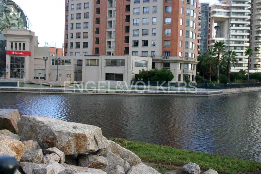 Waterfront view of modern buildings. A Santander bank is visible. Rocks and grass are in the foreground.