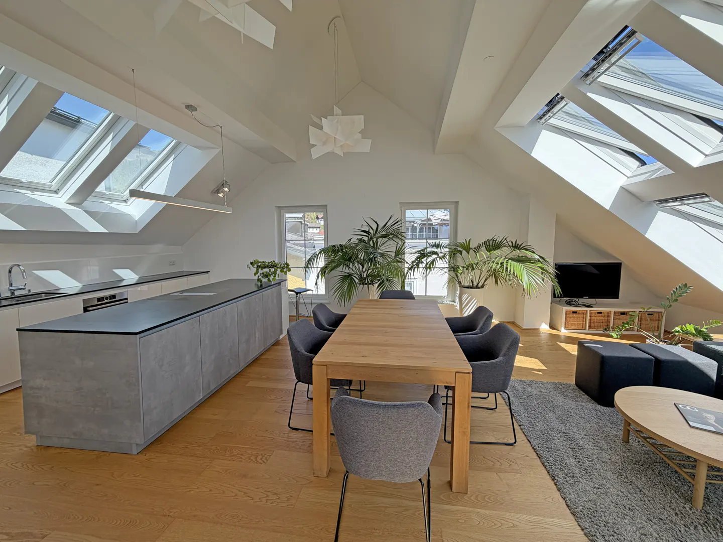 Bright, open-concept living space with skylights, a long kitchen island, a dining table with gray chairs, and a living area.