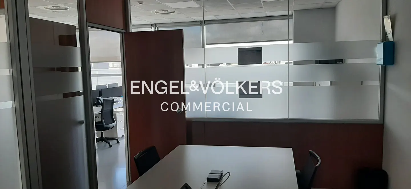 Modern office meeting room with a white table, black chairs, and glass partitions featuring the Engel & Völkers logo.