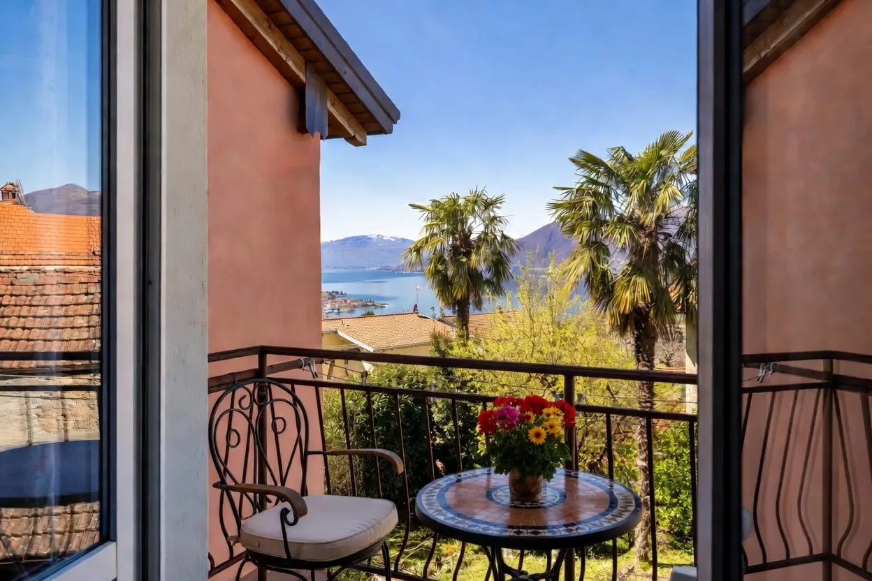 Balcony view with wrought iron furniture, a table with flowers, and a scenic view of a lake, mountains, and palm trees.