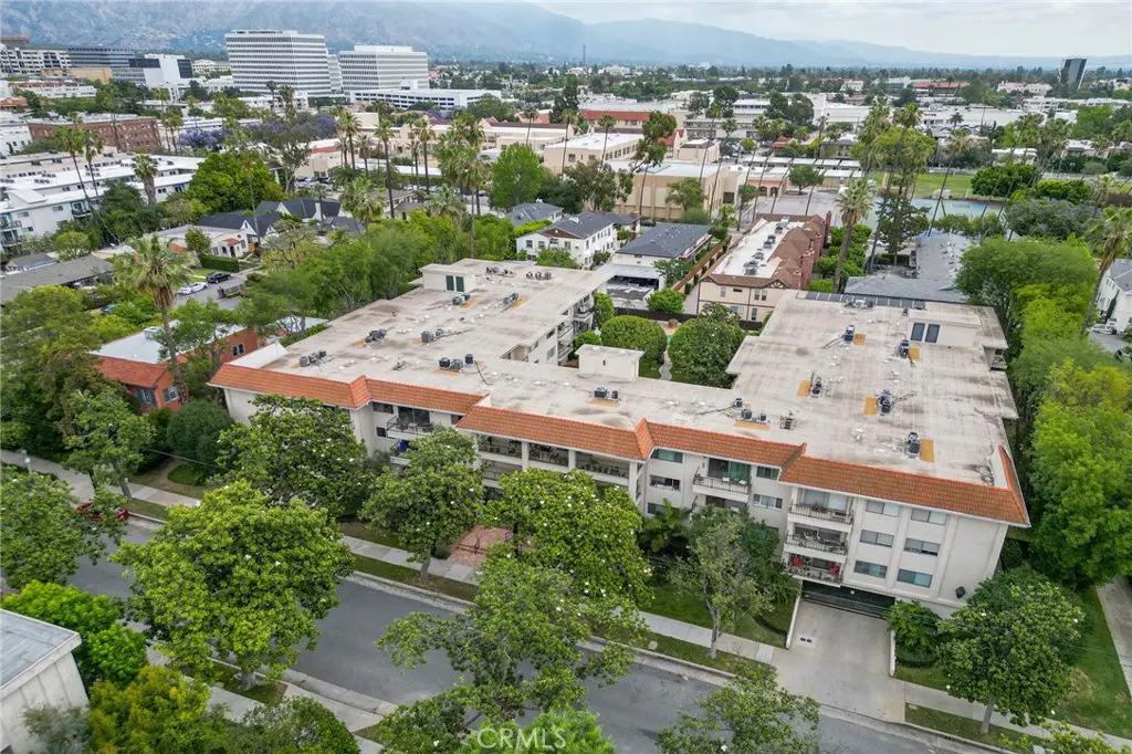 Aerial view of a multi-story apartment building with a red tile roof, surrounded by green trees and other buildings.
