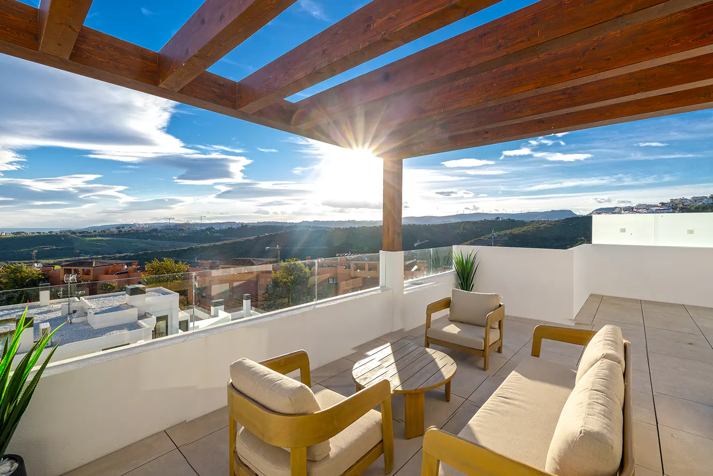 A sunny patio with wood furniture, a table, and a view of rolling hills under a blue sky.