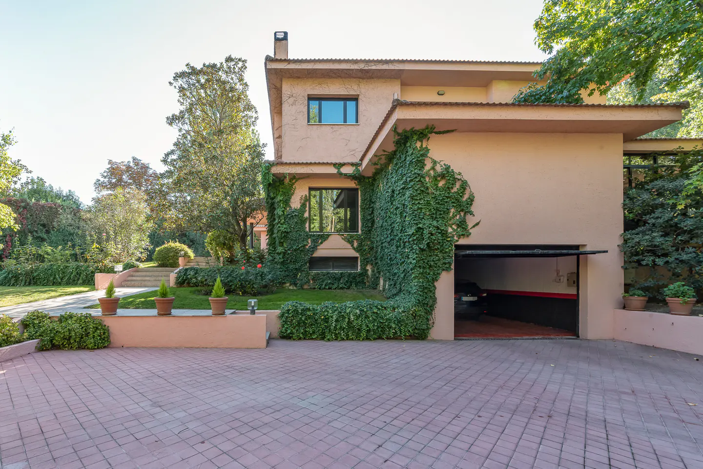Two-story peach house with an open garage door and brick driveway. Green ivy climbs the walls.