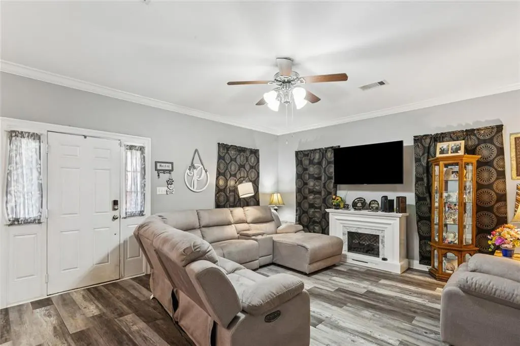 Living room with gray walls, wood floors, and a beige sectional sofa. A white fireplace is under a flat screen TV. A ceiling fan hangs above.