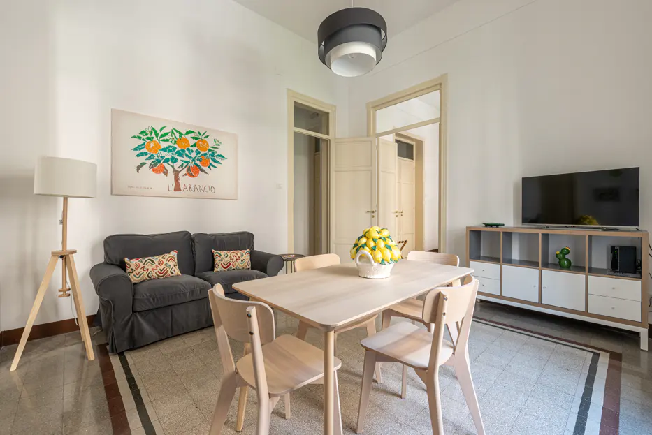Living room with gray sofa, wooden table with lemons, and TV. Orange tree art hangs on the white wall.