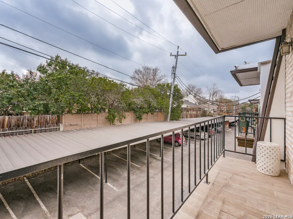 View from a balcony overlooking a covered parking area with cars, trees, and a cloudy sky in the background.