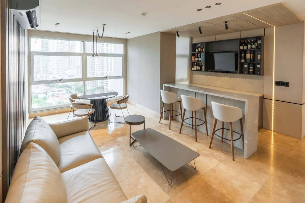 Living room with a bar, a beige sofa, a black table with four chairs, and a gray coffee table on a marble floor.