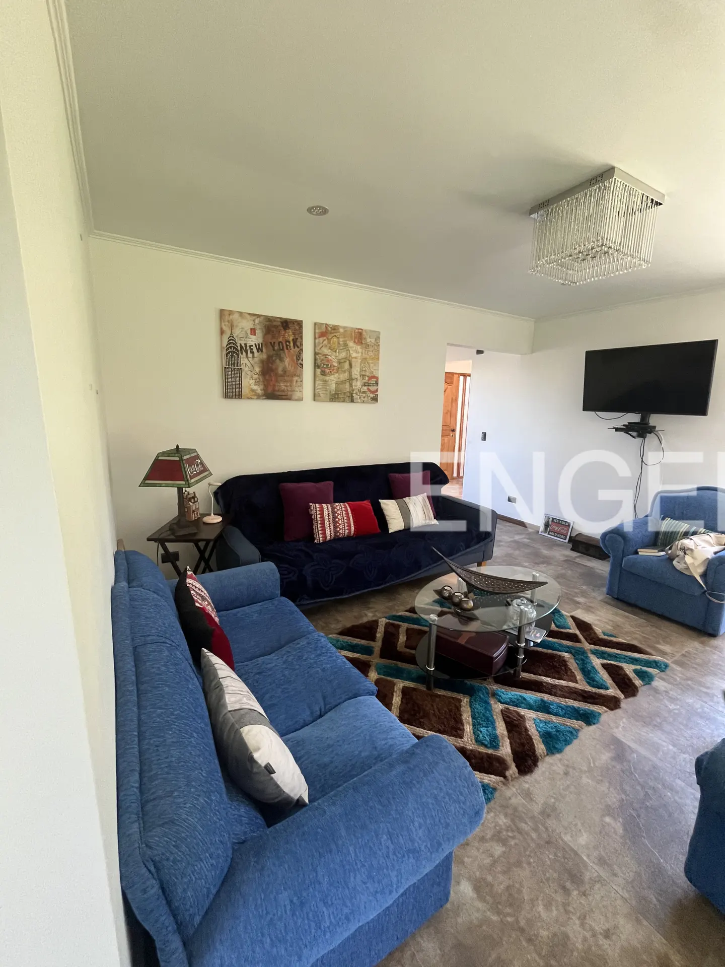 Living room with blue sofas, a dark blue futon, and a brown and blue rug. A TV hangs on the wall, and art hangs above the futon.