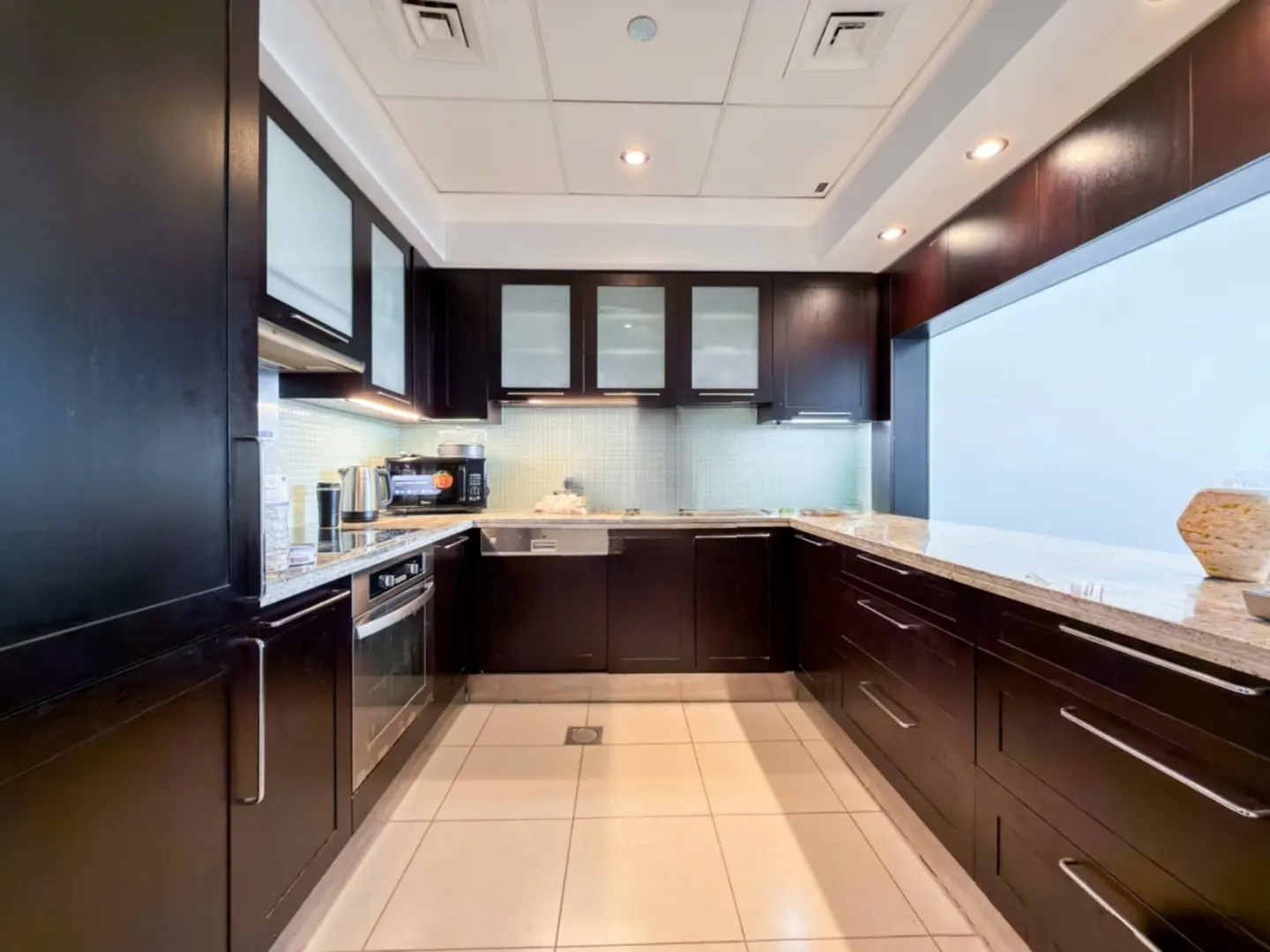 Modern U-shaped kitchen with dark wood cabinets, light granite countertops, stainless steel appliances, and tiled floors.
