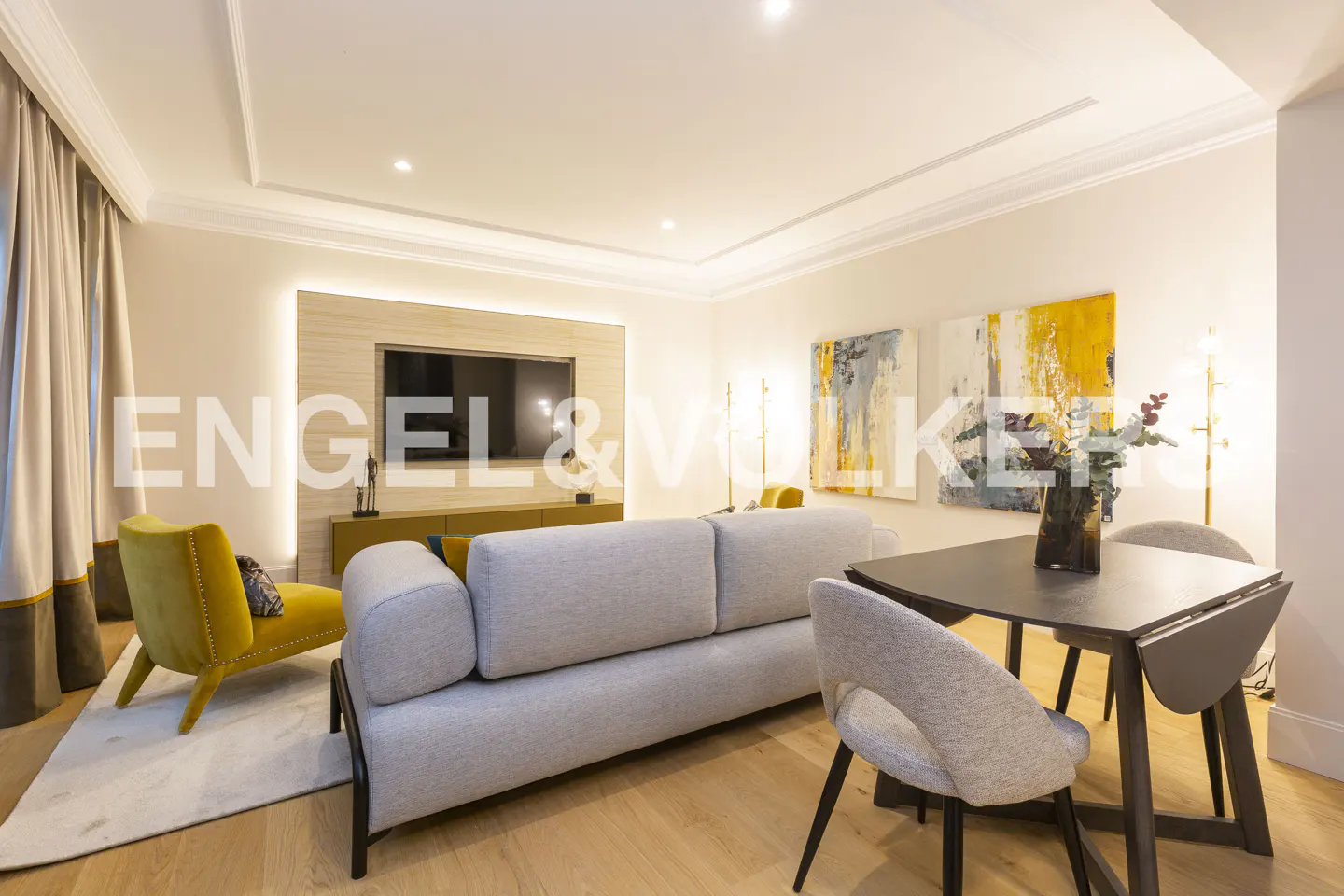 Living room with a gray sofa, yellow chaise lounge, and a dark wood dining table with gray chairs. Abstract art hangs on the wall.