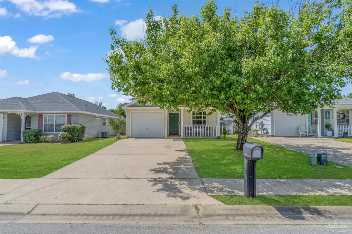 A single-story beige house with a green door and a large tree in the front yard.