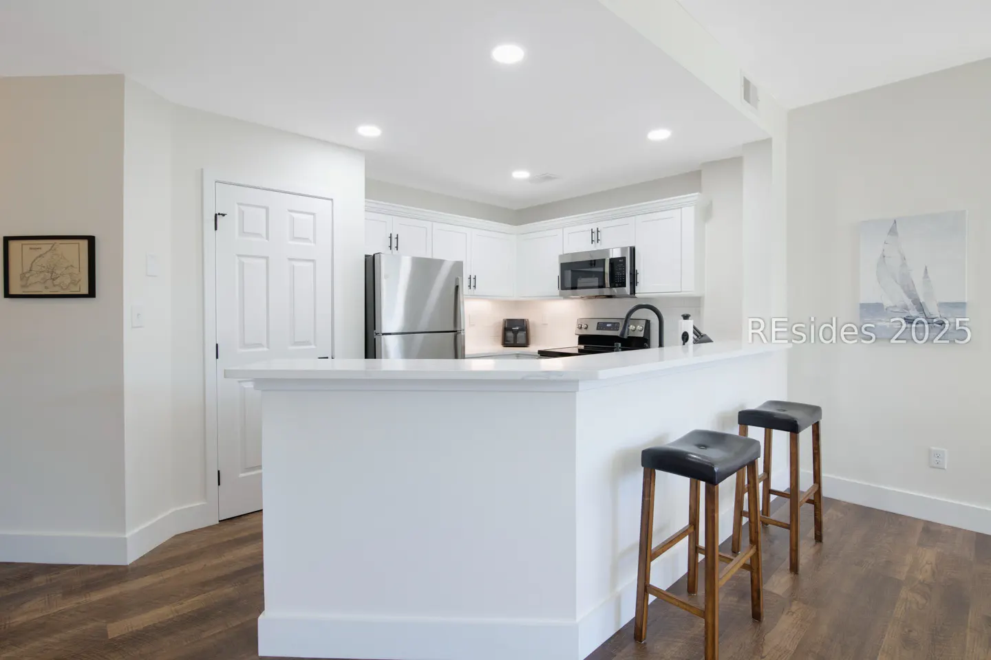 Bright, modern kitchen with white cabinets, stainless steel appliances, and a white countertop island with two black leather bar stools.