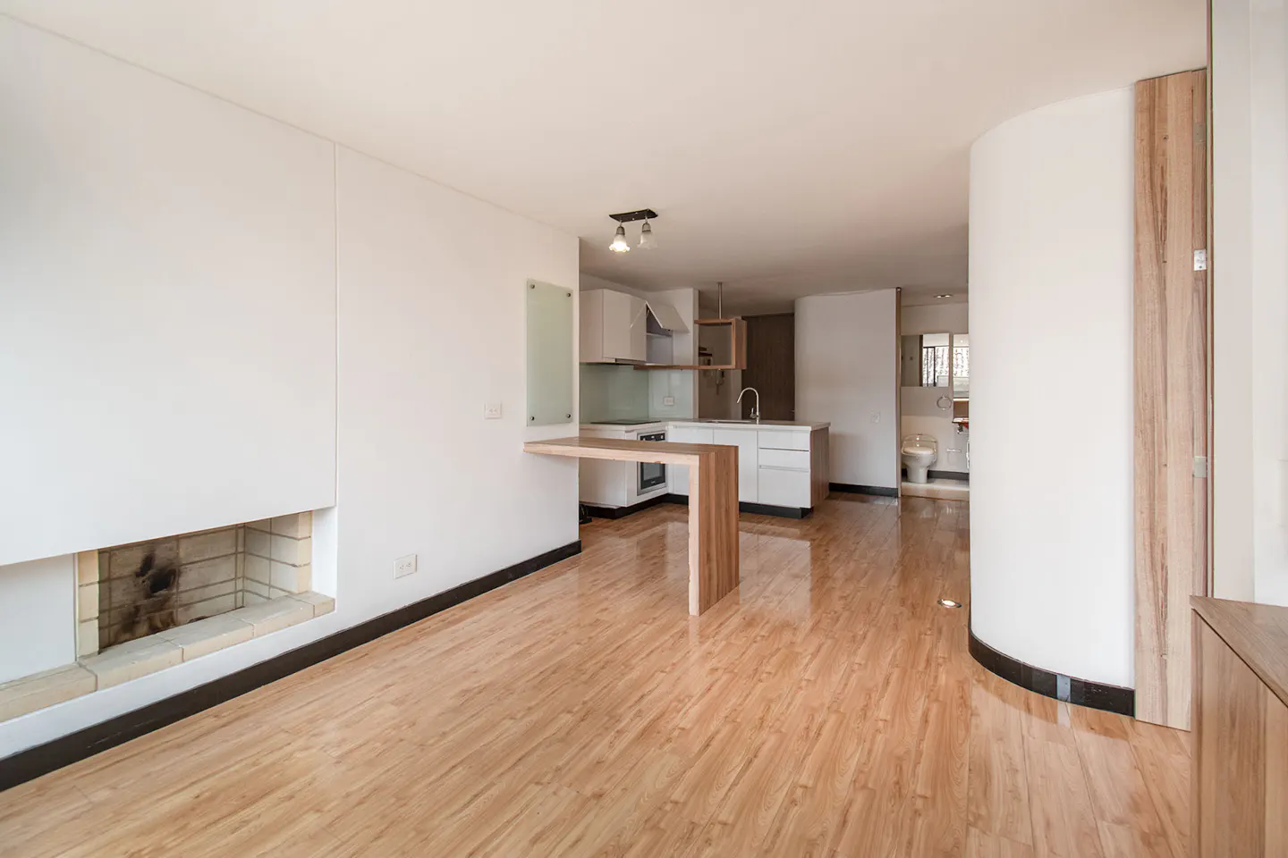Bright, modern apartment interior with wood floors, white walls, and an open kitchen. A fireplace is on the left.
