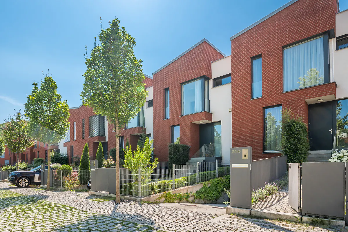 Row of modern brick townhouses with gray fences and green trees under a clear blue sky.