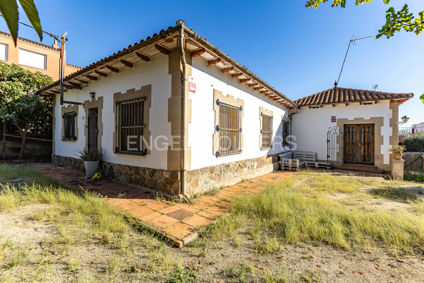 Exterior view of a white, one-story house with stone accents, a red tile roof, and a small yard.