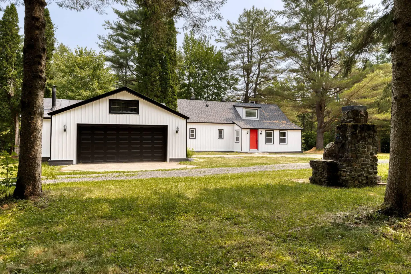 A white house with a red door and black trim, next to a matching garage, sits on a green lawn.