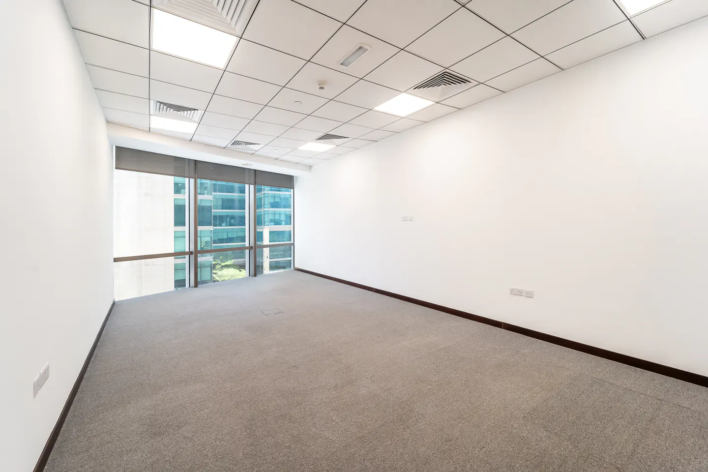 Empty office space with gray carpet, white walls, and a large window showing a city view.