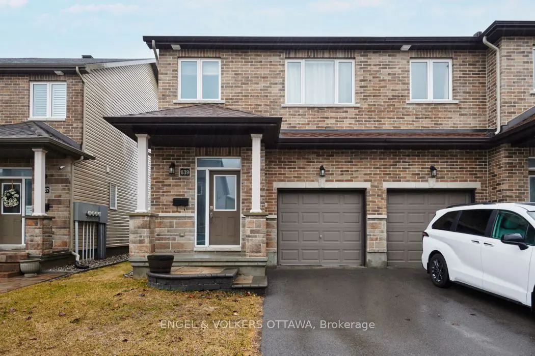 A two-story brick townhouse with a brown door and two-car garage. A white minivan is parked in the driveway.