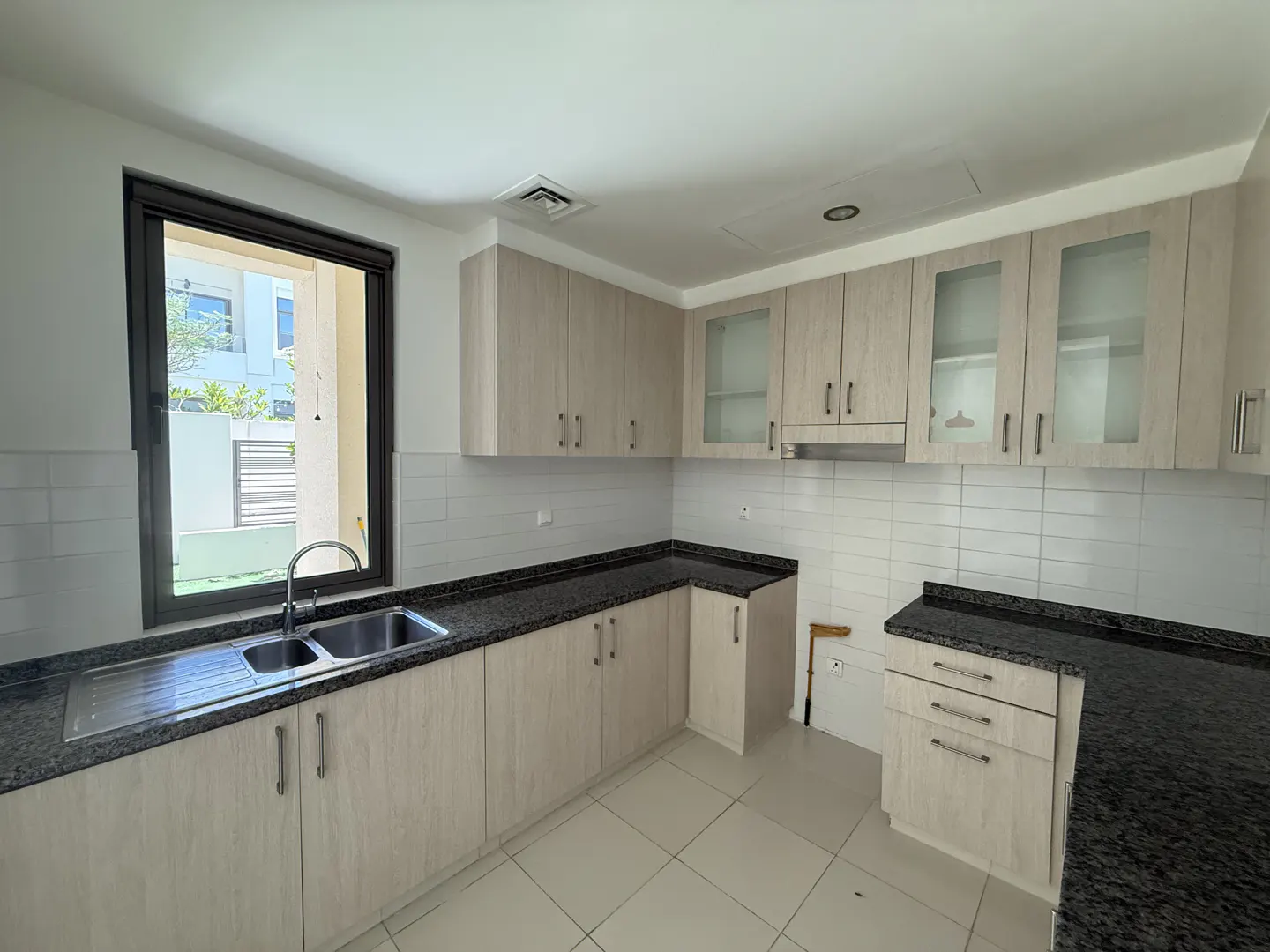 Bright kitchen with light wood cabinets, dark granite countertops, and a stainless steel sink under a window.