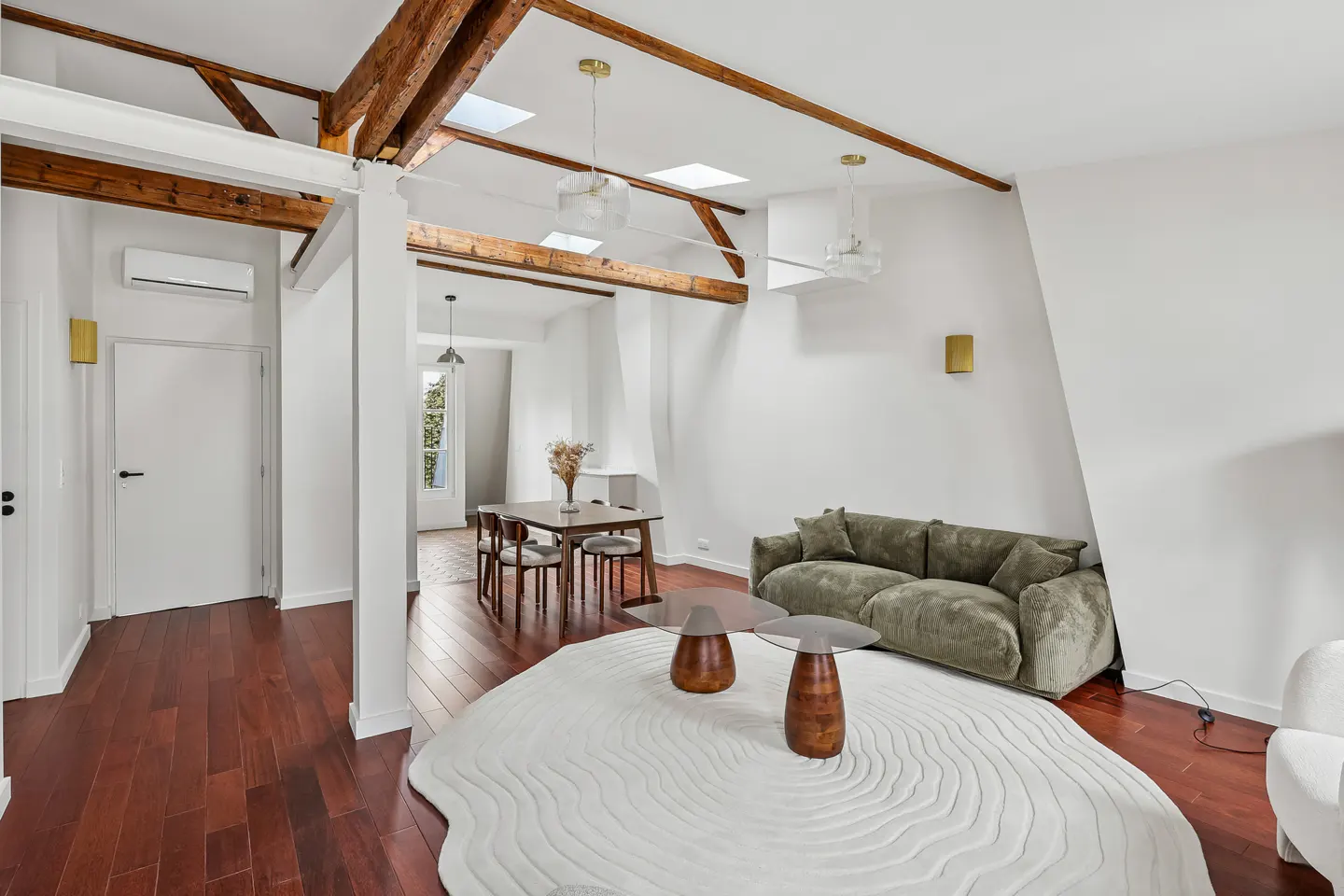 Modern living room with exposed wooden beams, olive green sofa, two round coffee tables, and a textured white area rug.