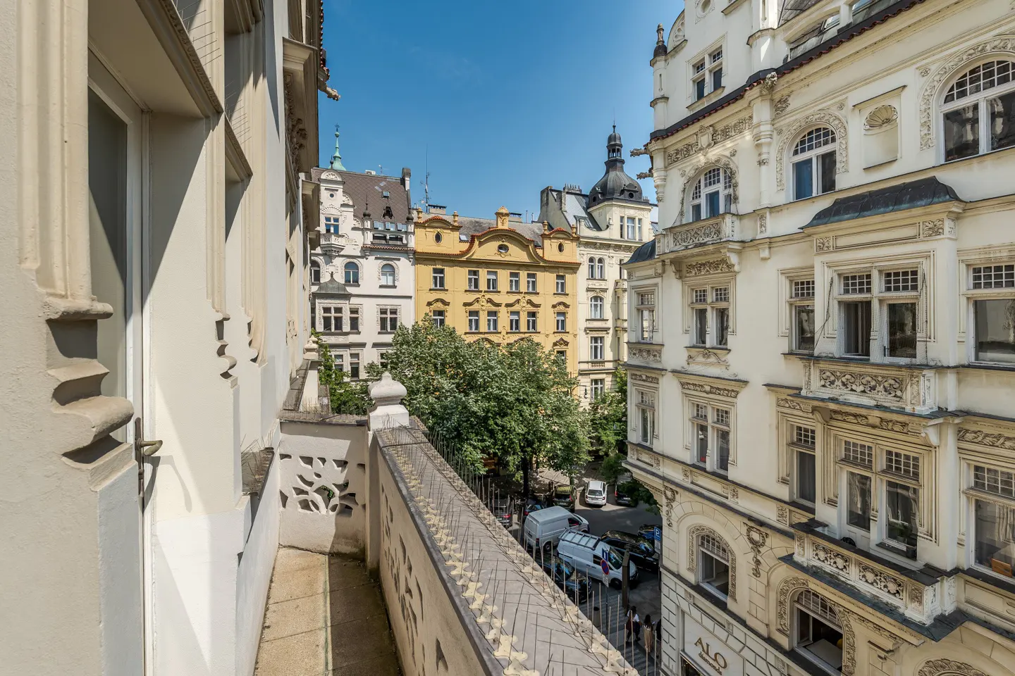 View from a balcony overlooking a European city street with ornate buildings and a blue sky.