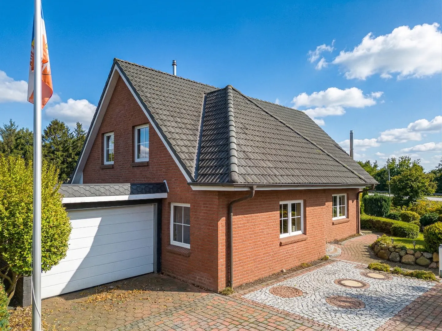 A red brick house with a gray roof, white trim, and a white garage door on a sunny day.