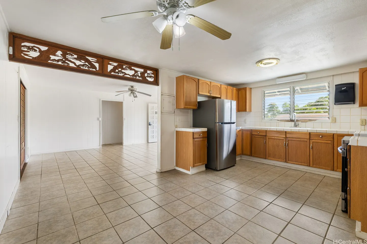 Kitchen with light wood cabinets, stainless steel refrigerator, tiled floors, and a decorative wood room divider.