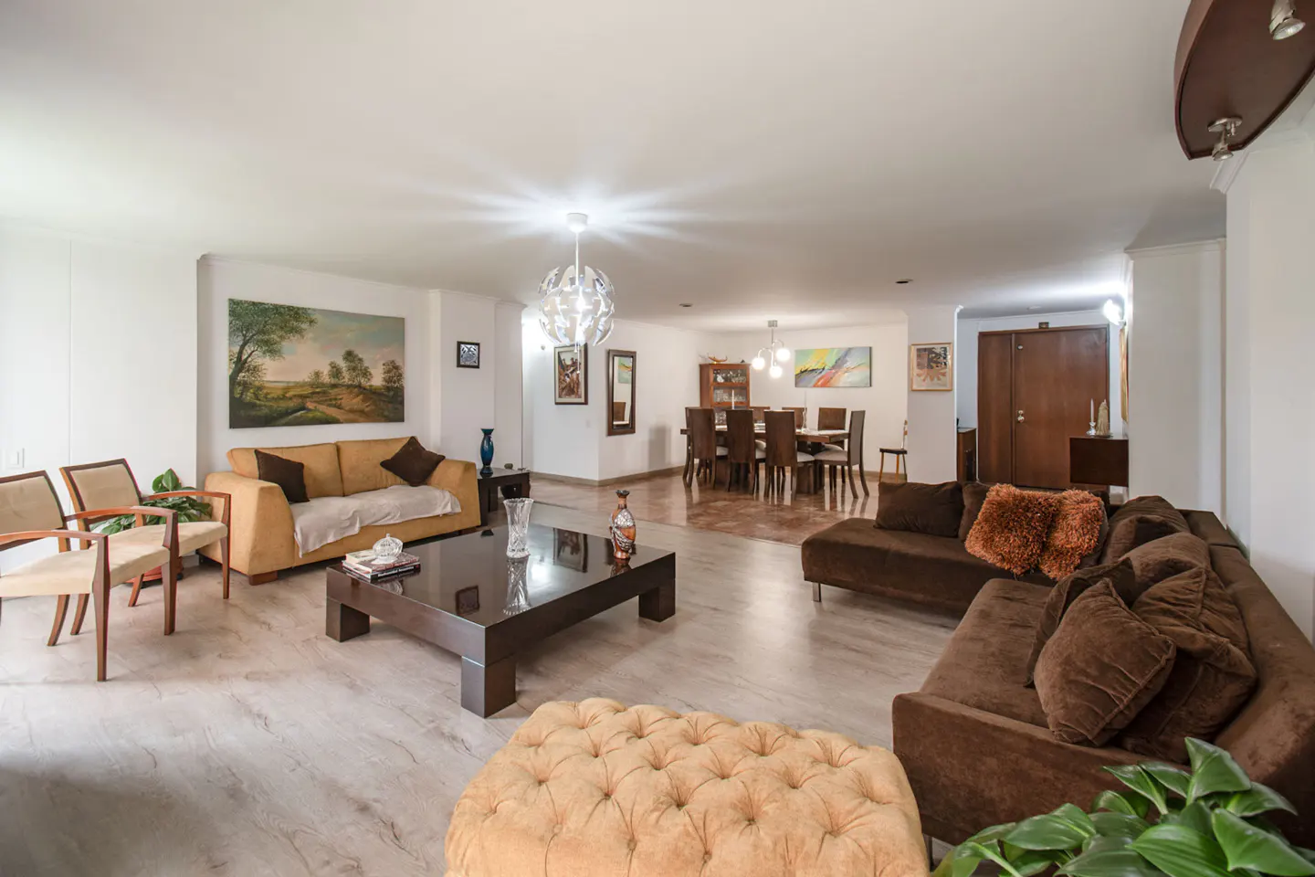 Bright, open-concept living and dining area with tan and brown sofas, a dark coffee table, and a dining table with brown chairs.