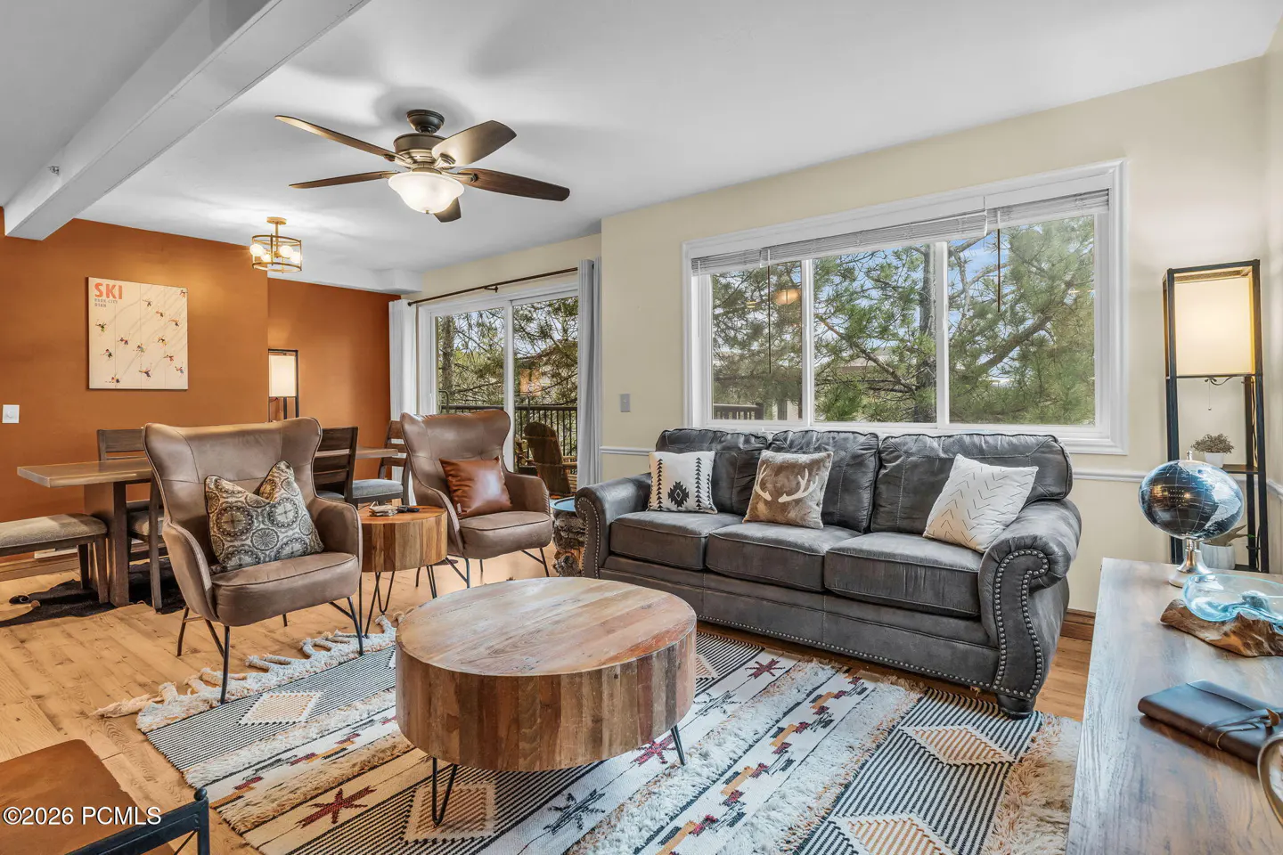 Living room with brown leather chairs, gray sofa, and wood coffee table on a patterned rug. A ski map hangs on the orange wall.