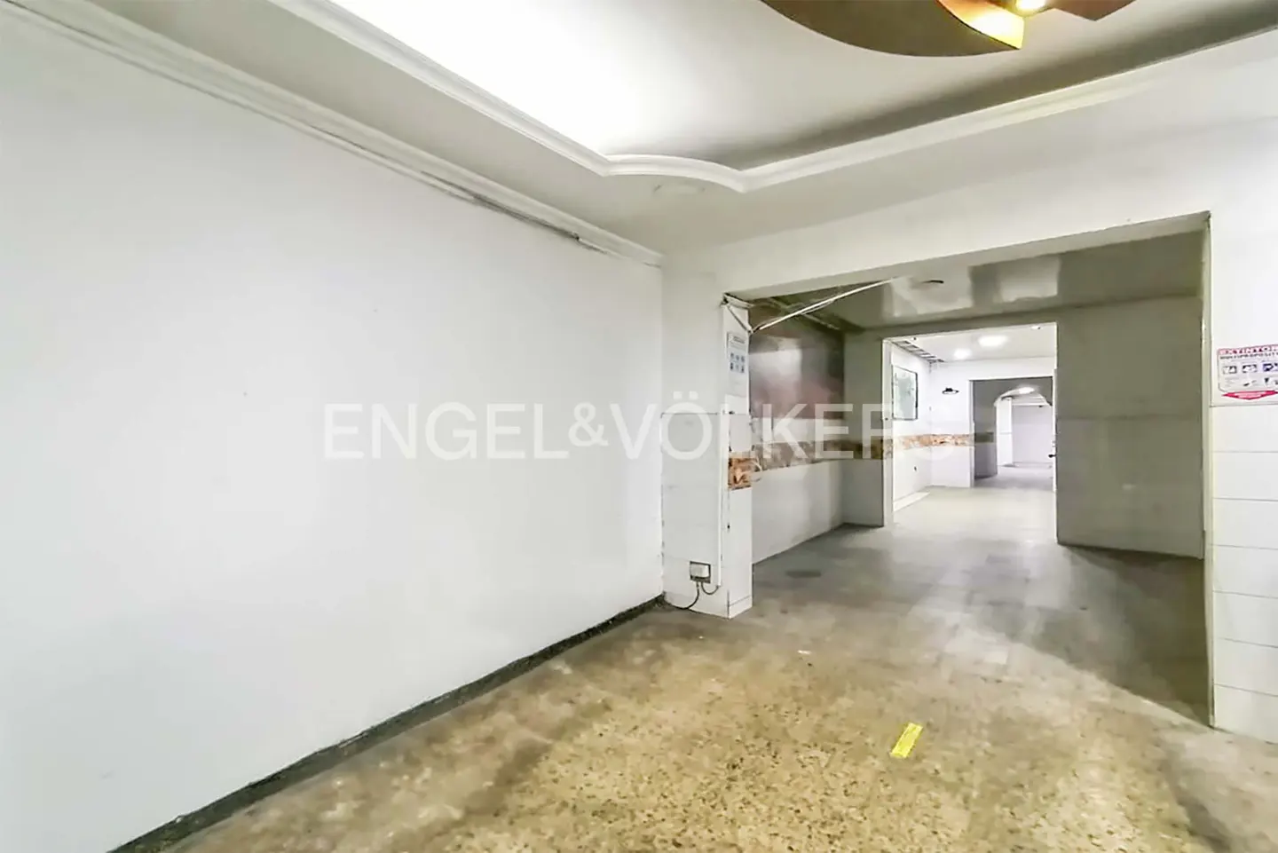 Empty room with white walls, a speckled floor, and an open doorway leading to another room. Engel & Völkers logo on the wall.