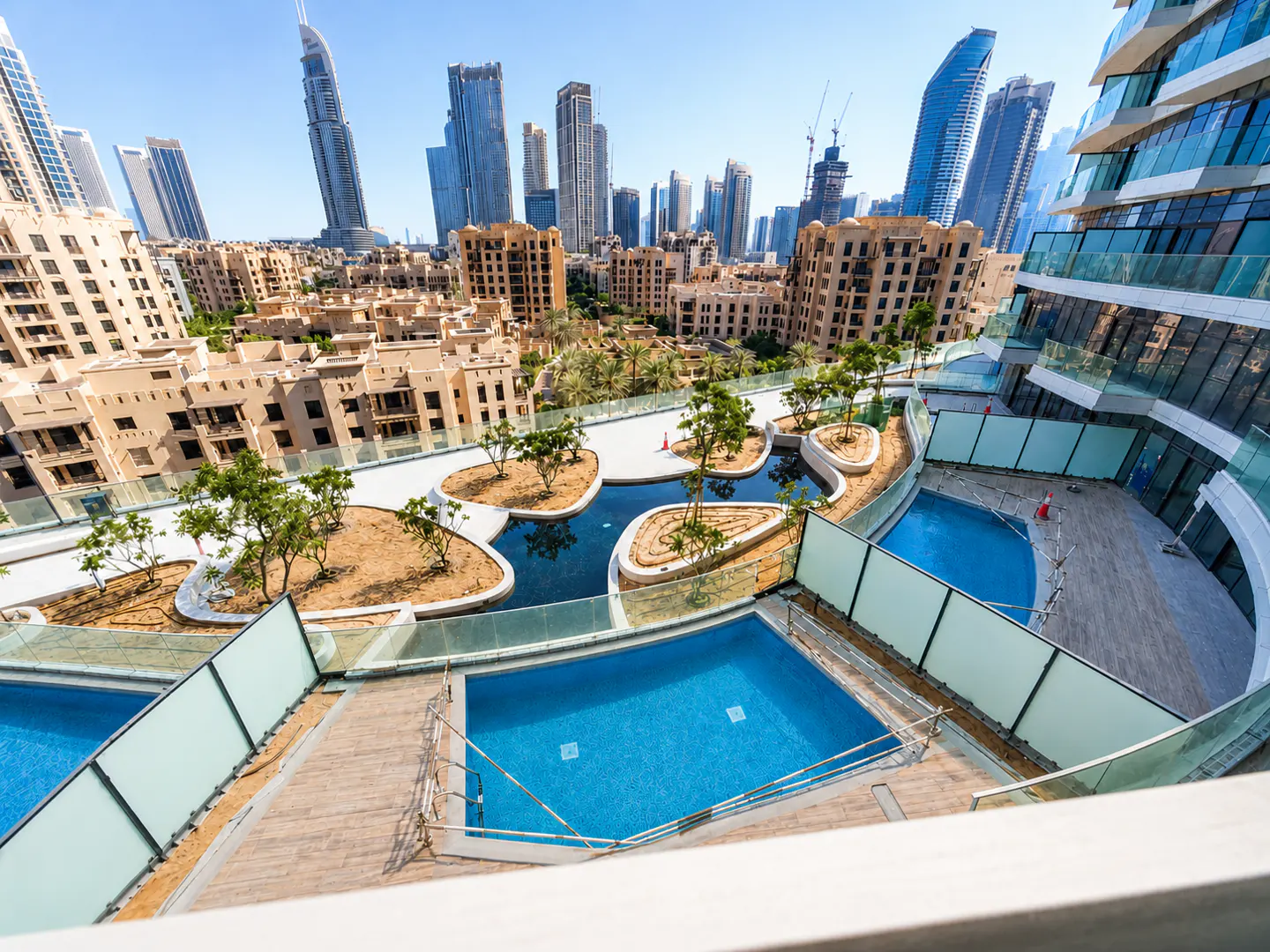 View of Dubai skyline with pools and landscaping in foreground. Modern buildings and blue sky in the background.