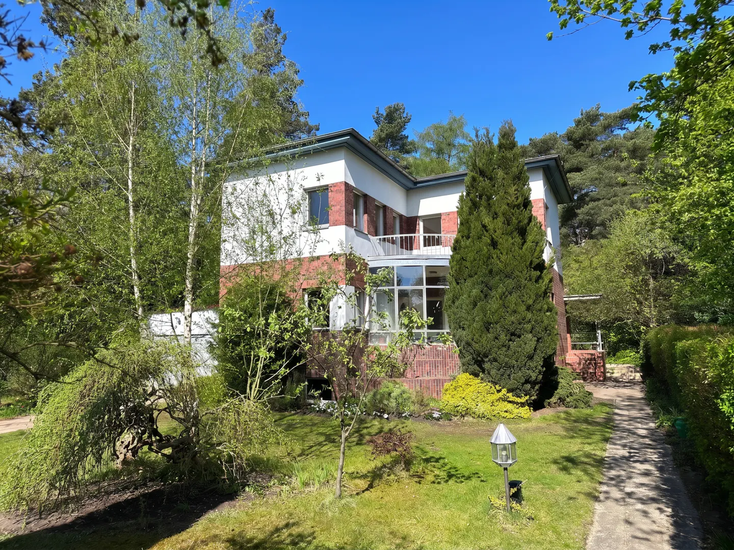 Two-story house with white and red brick exterior, surrounded by green trees and lawn under a blue sky.