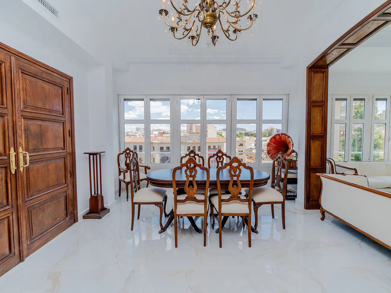 Elegant dining room with a dark wood table, six chairs, a crystal chandelier, and large windows overlooking a city view.