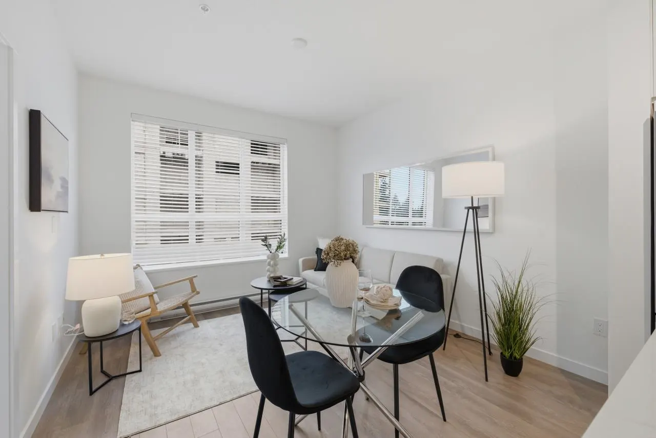 Bright, modern living room with a glass table, black chairs, and a white sofa. A large window with blinds lets in natural light.