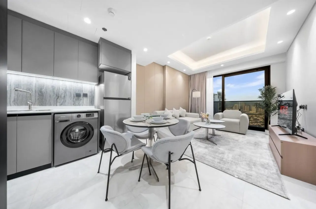 Modern apartment interior with gray cabinets, stainless steel appliances, round dining table, and living area with city view.