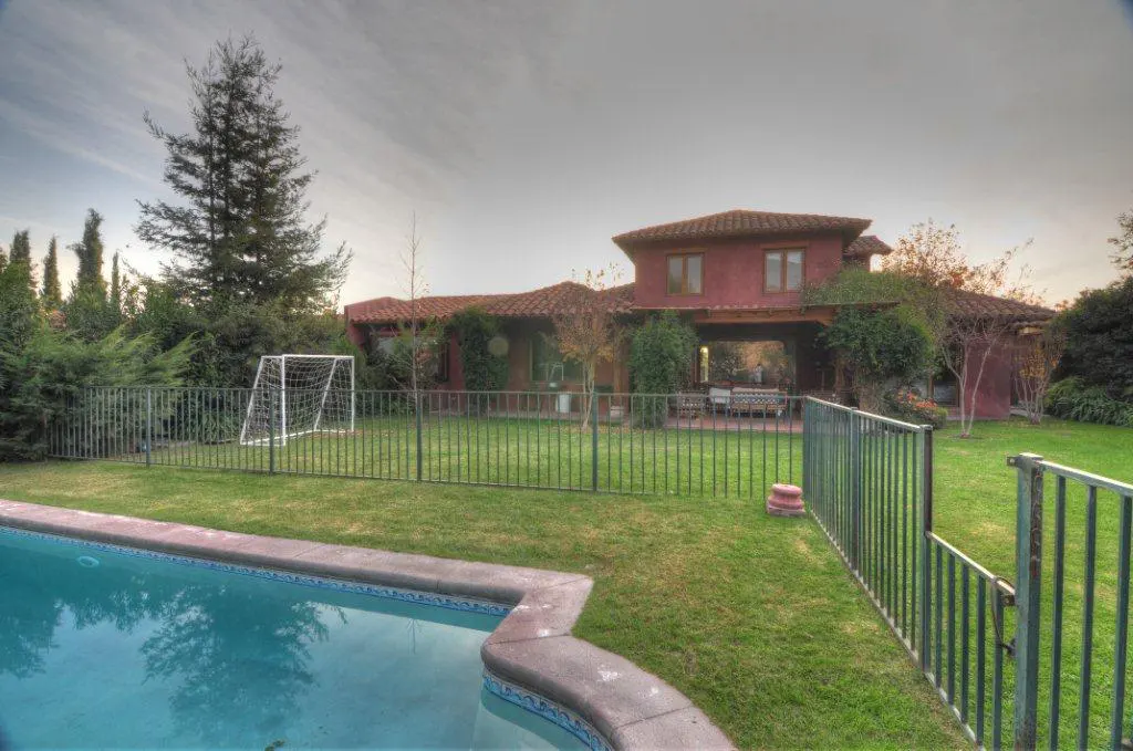 Backyard view of a red house with a terracotta roof, green lawn, pool, and soccer goal.