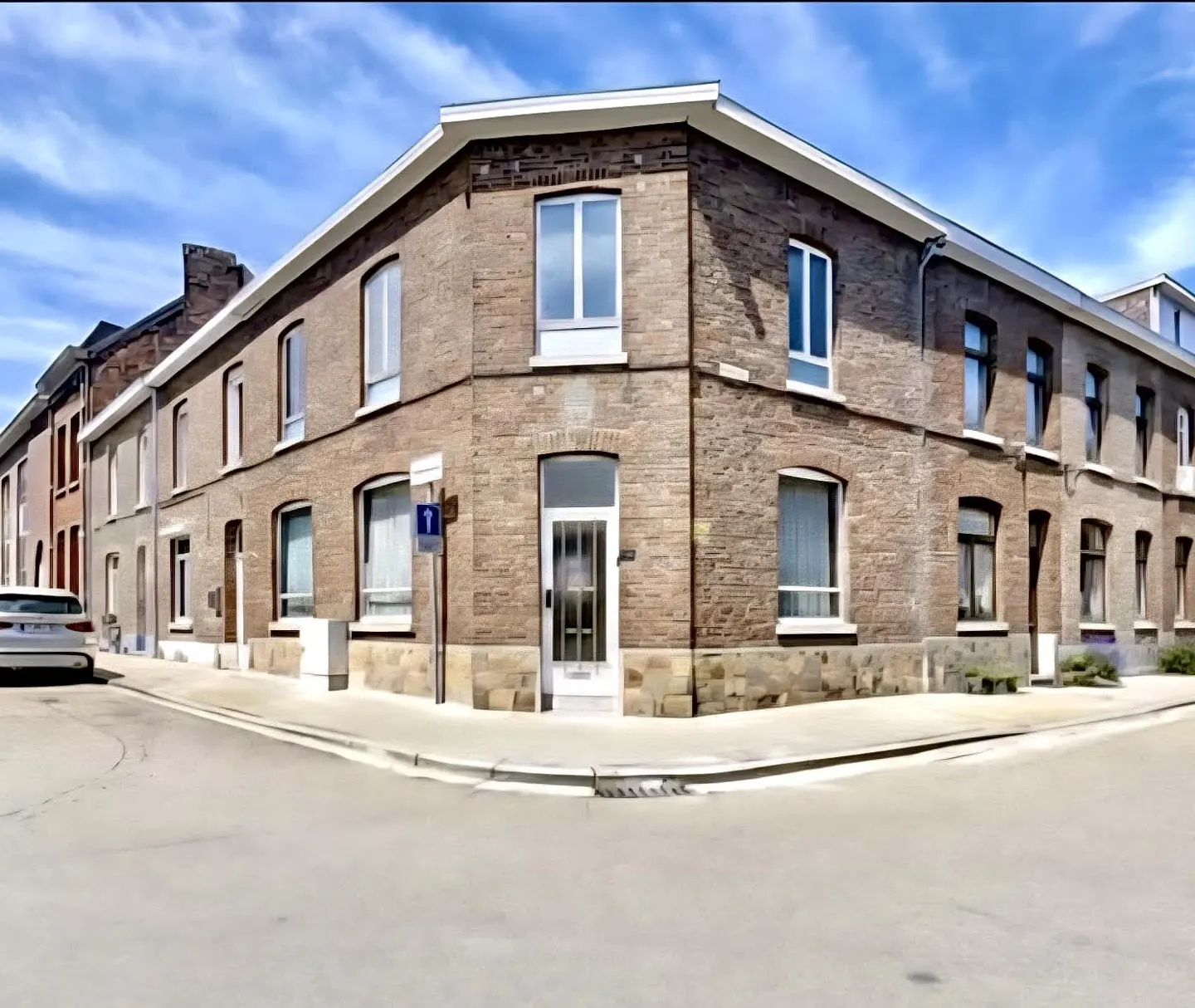 A corner view of a two-story brick building with white trim and a white door under a blue sky.