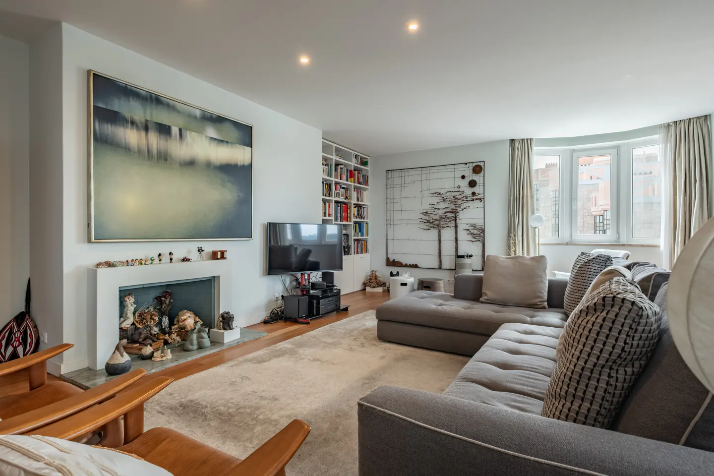 A modern living room with a gray sectional sofa, a fireplace with art, and a large abstract painting.