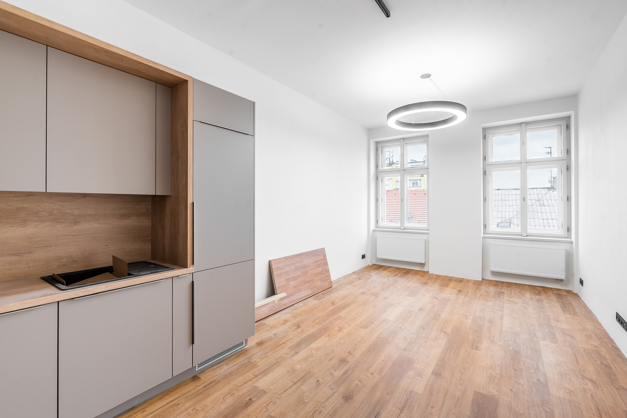 Modern kitchen with grey cabinets, wood accents, and light wood flooring, featuring two windows and a circular ceiling light.
