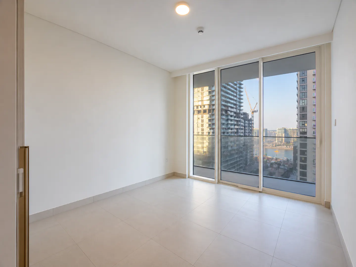 Empty room with white walls and tile floor. Sliding glass doors reveal a city view with skyscrapers and a body of water.