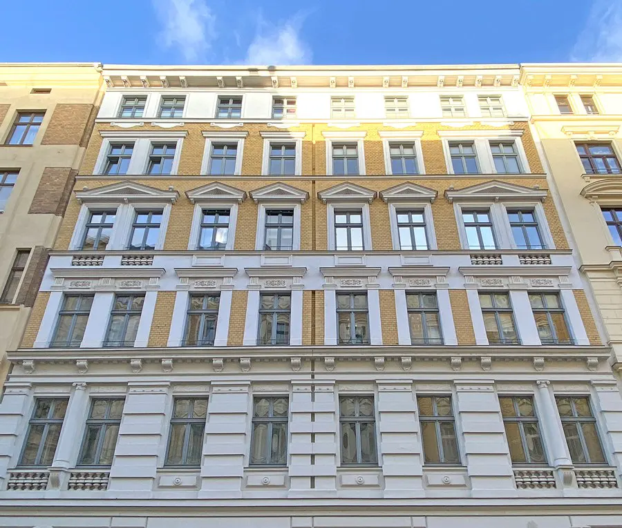 A low-angle shot of a yellow and white apartment building with many windows under a blue sky.