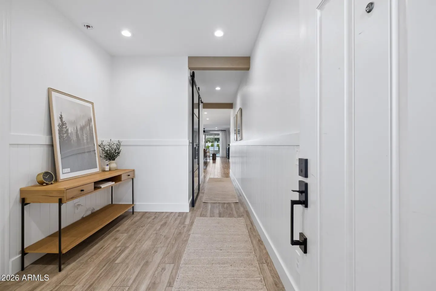 Bright hallway with white walls, wood floors, and a console table with a framed print. A sliding barn door leads to another room.