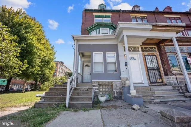 Exterior view of row houses with concrete steps leading to white doors, gray and brick facades, and a green bay window.