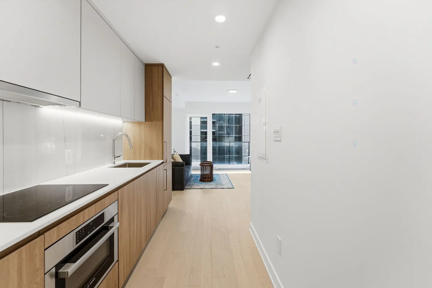 Modern condo interior with white cabinets, wood accents, stainless steel appliances, and a view of the city.