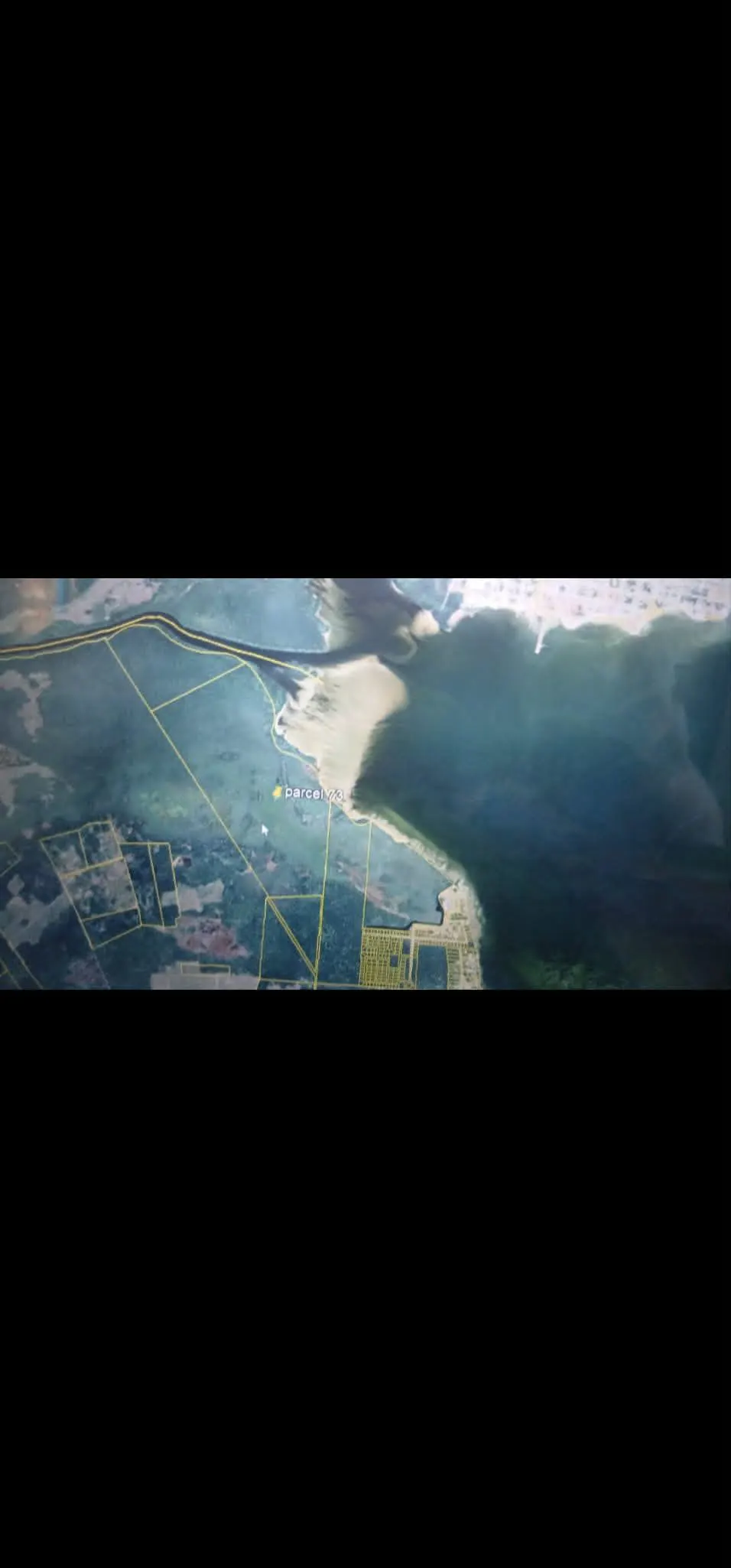 Aerial view of land parcels near a body of water, with green land and blue water.