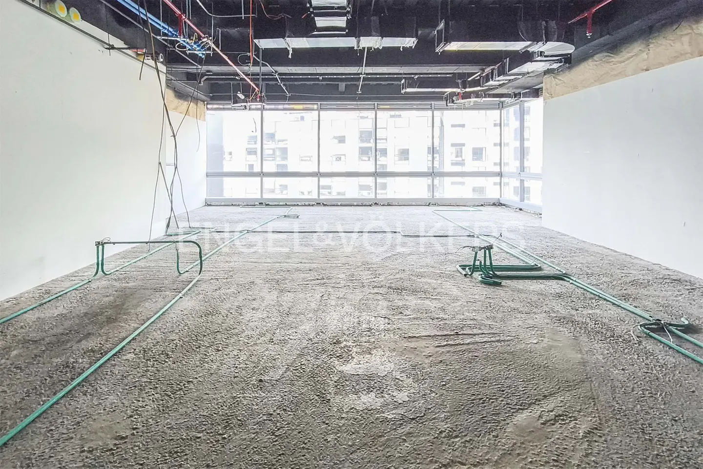 Unfinished room with concrete floor, white walls, and large window. Green pipes run across the floor. Exposed ceiling with pipes and ductwork.