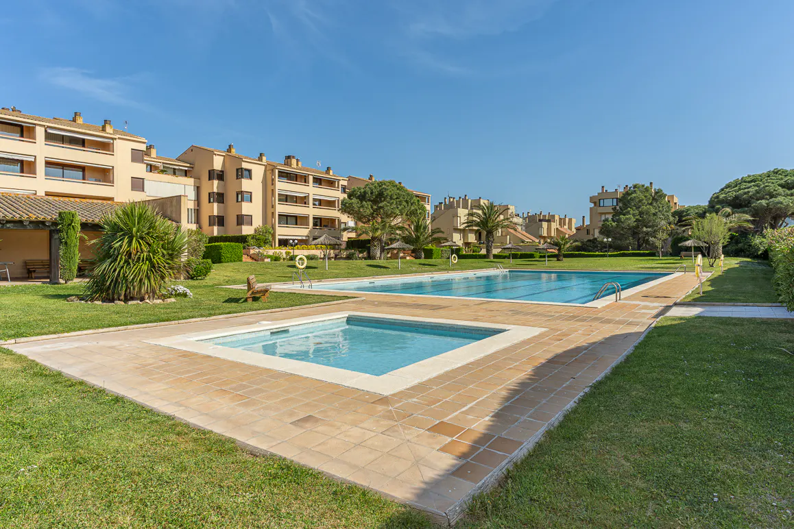 Exterior view of a complex with a pool, jacuzzi, and tan buildings under a blue sky.